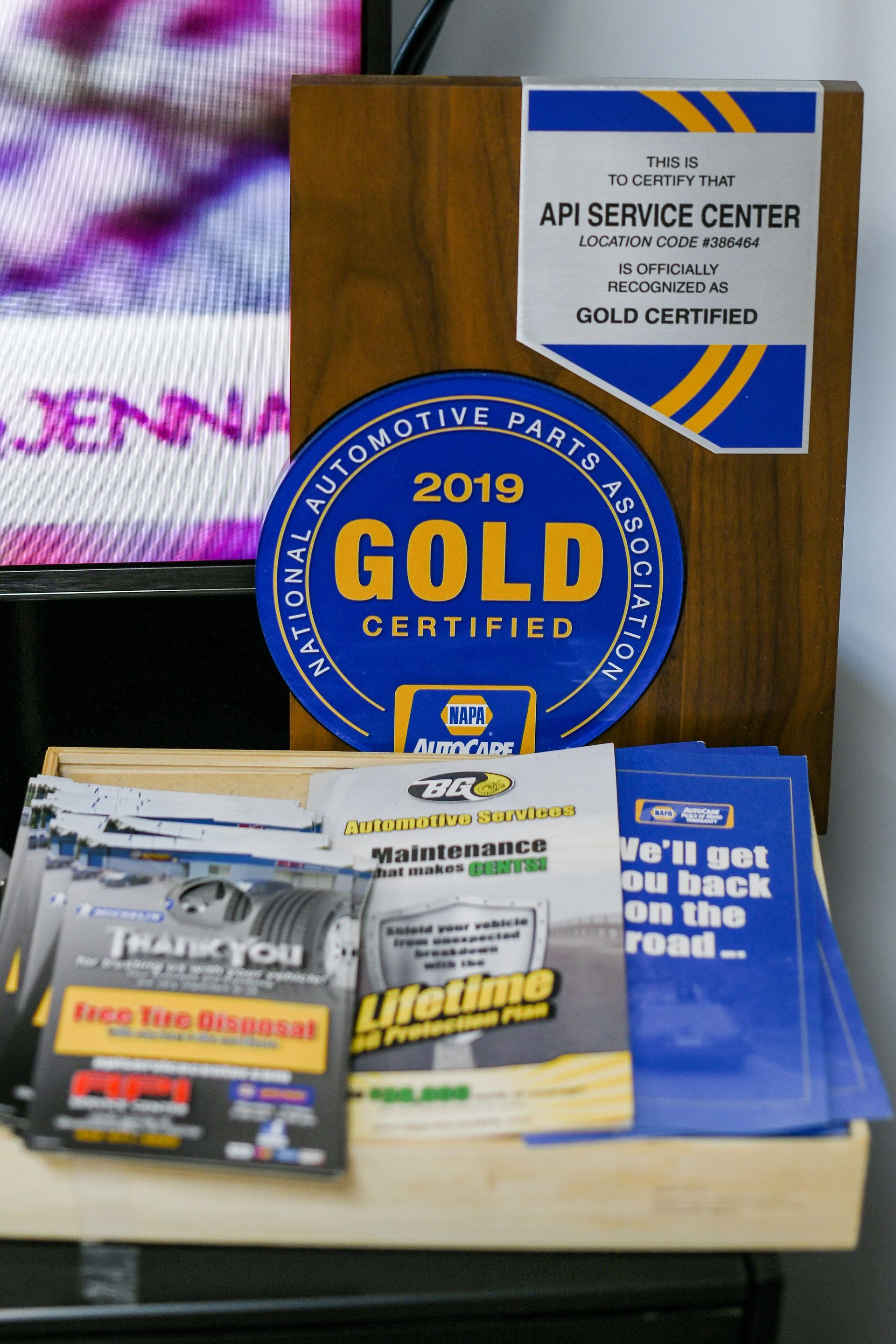 Awards and brochures on a desk, with a gold certified plaque and a service center sign behind them