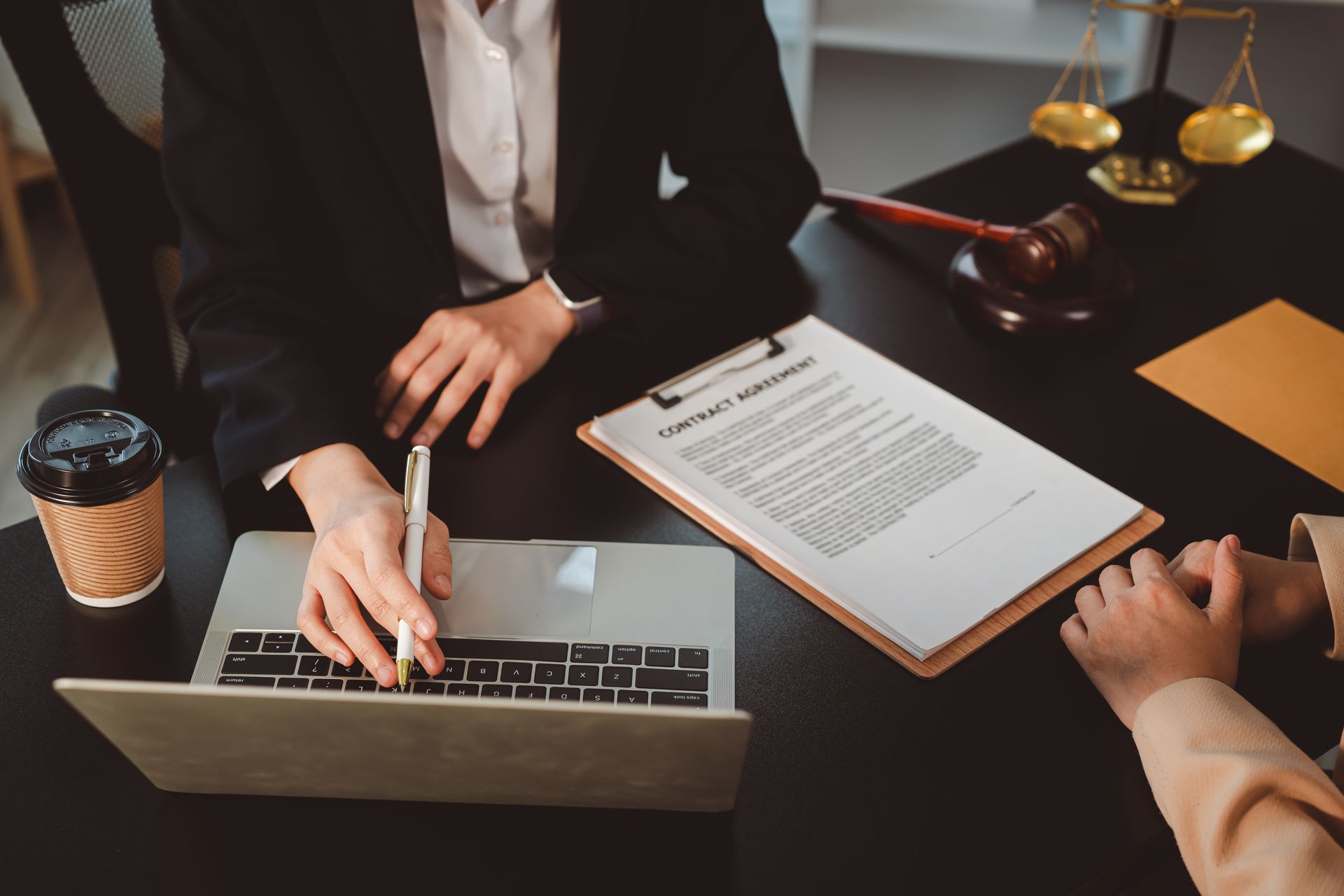 A business law lawyer is indicating to a client where to sign after reviewing business documents. Business law lawyer reviewing a contract agreement with a client at a desk.