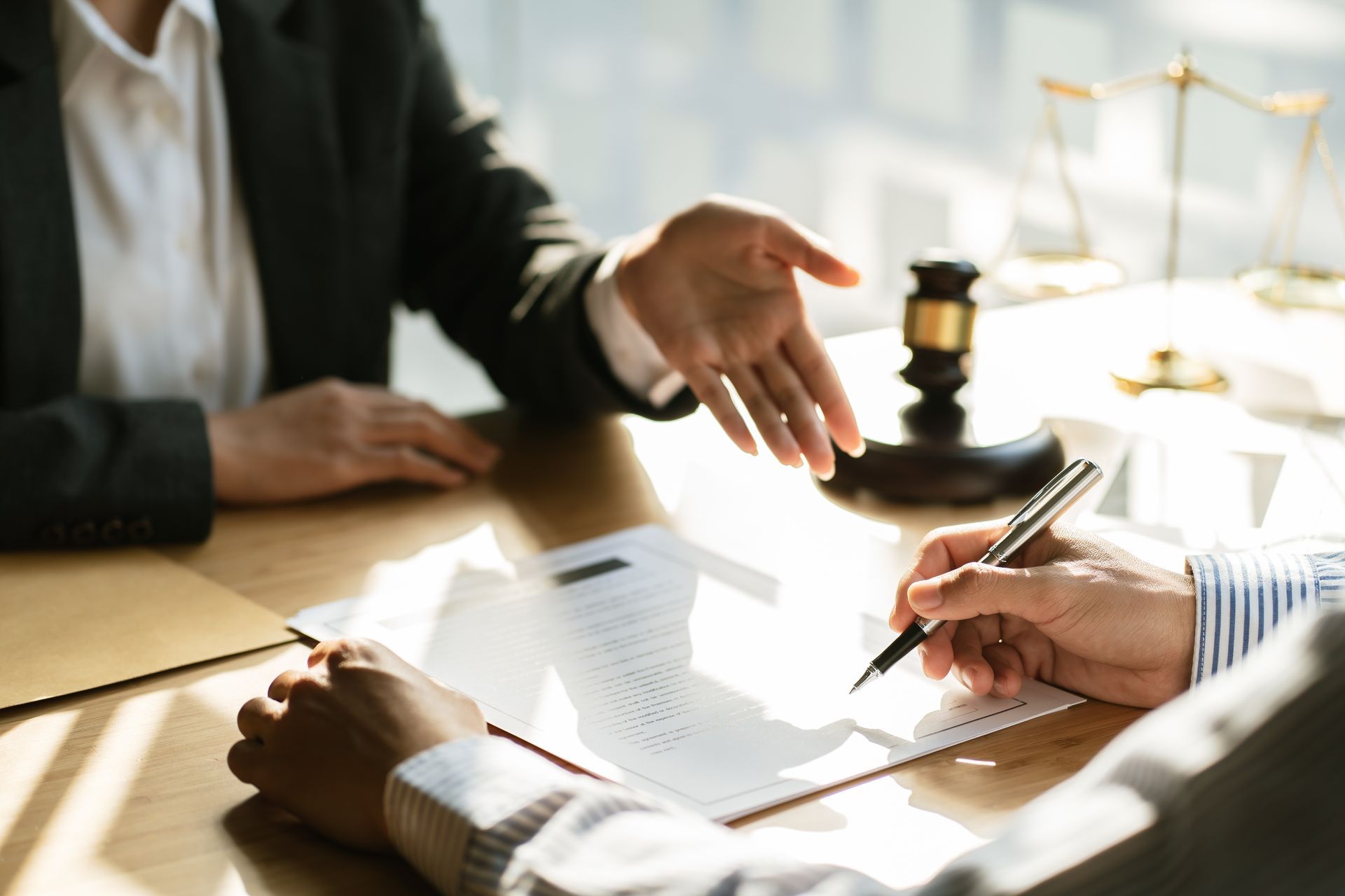 Solicitor pointing to a document as a client signs beside a gavel and scales of justice.