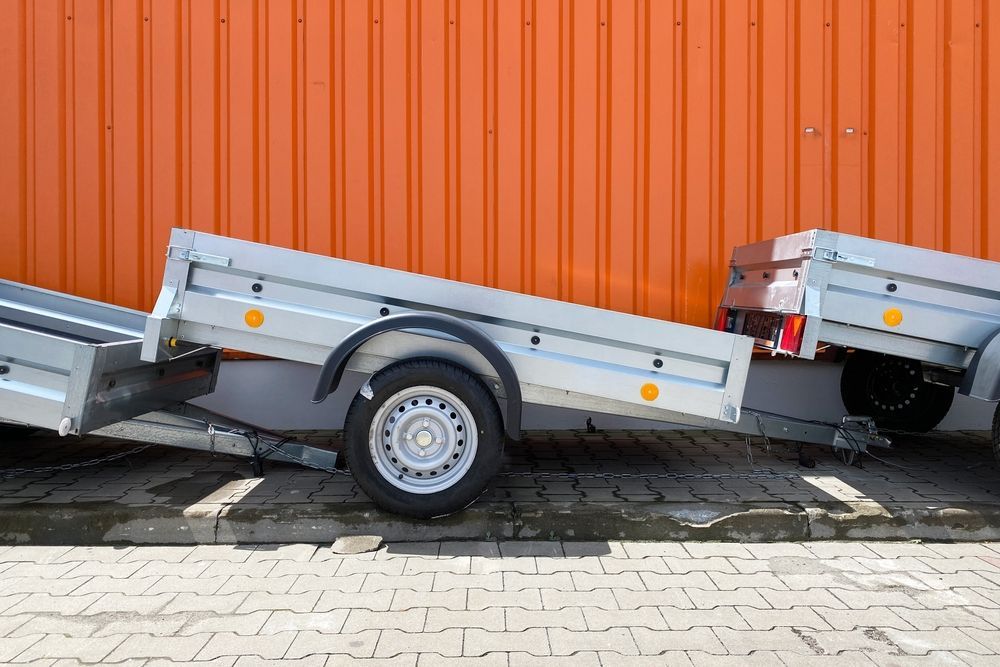 Three silver utility trailers parked in front of an orange corrugated wall.
