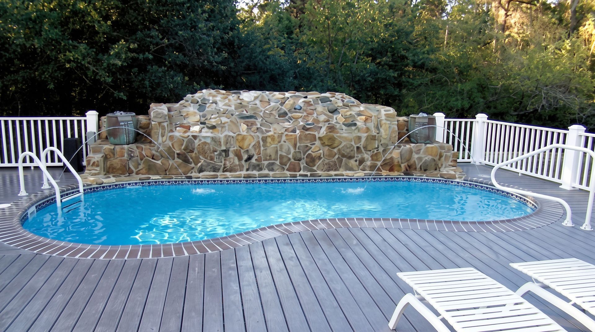 Backyard pool with turquoise water, white railings, and a stone waterfall wall at the far end