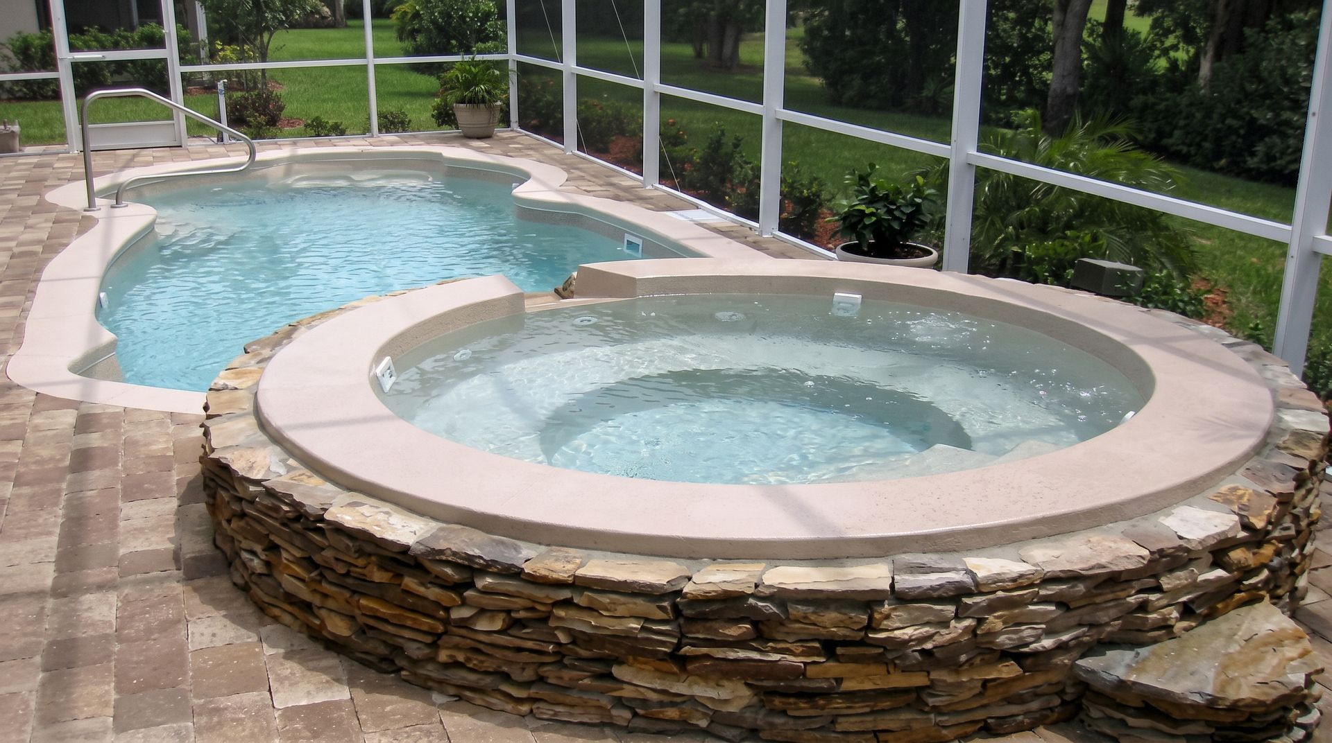 Circular stone hot tub beside a kidney-shaped pool in a backyard patio setting