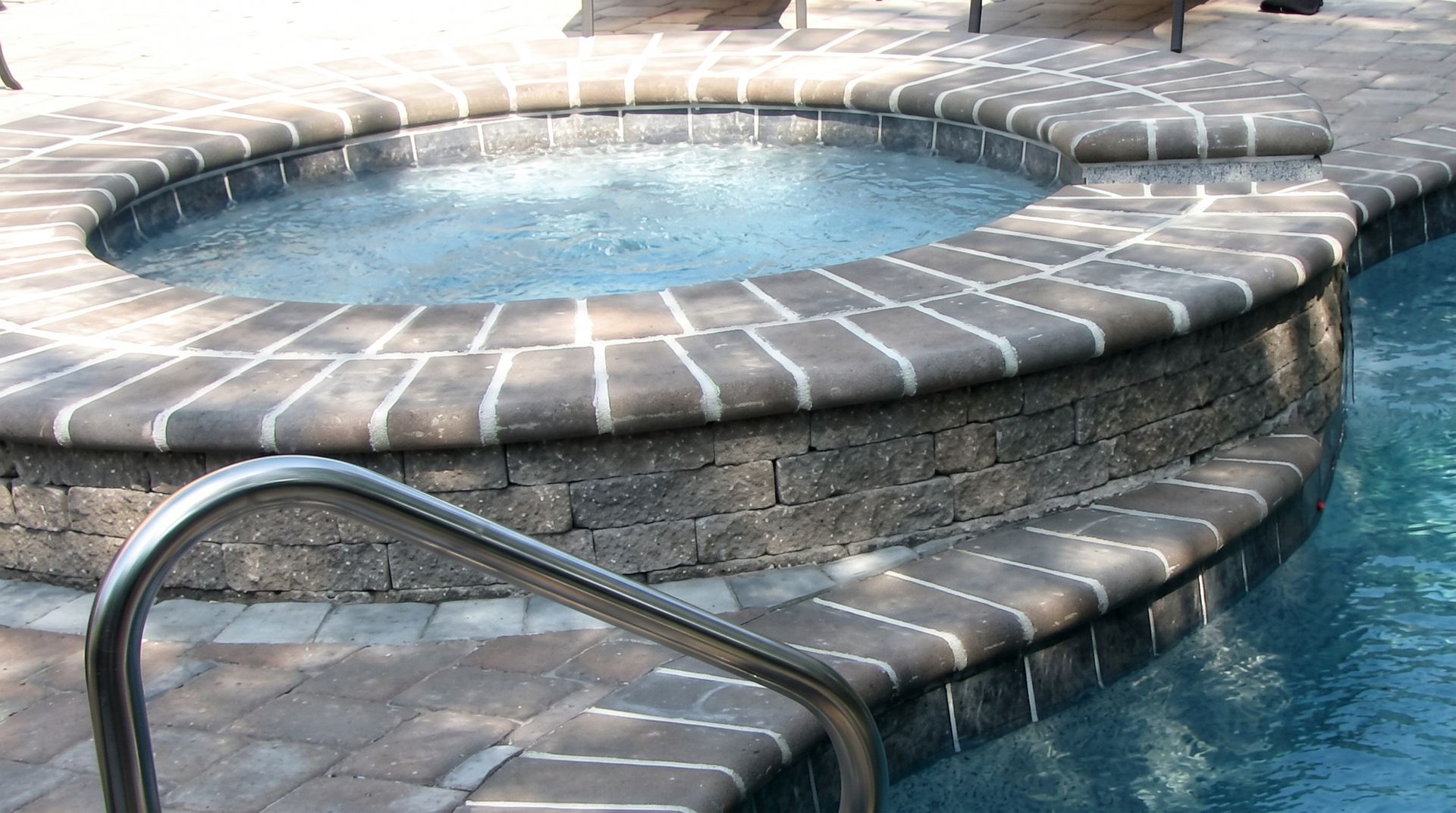 Curved stone pool steps with a metal handrail leading into a blue outdoor pool