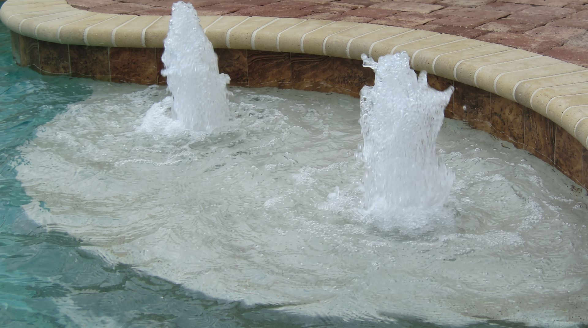 Two water jets bubbling in a turquoise pool beside a curved stone edge
