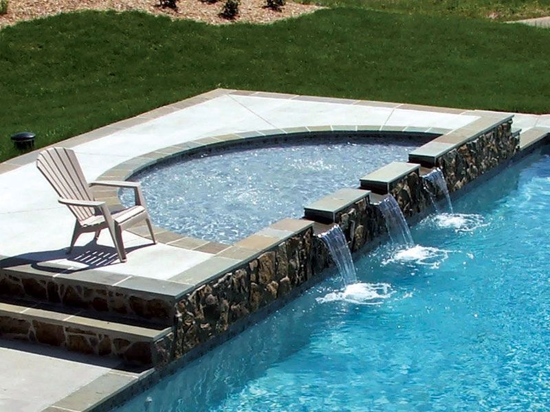 Backyard pool with stone waterfall, blue water, and a lounge chair on the deck