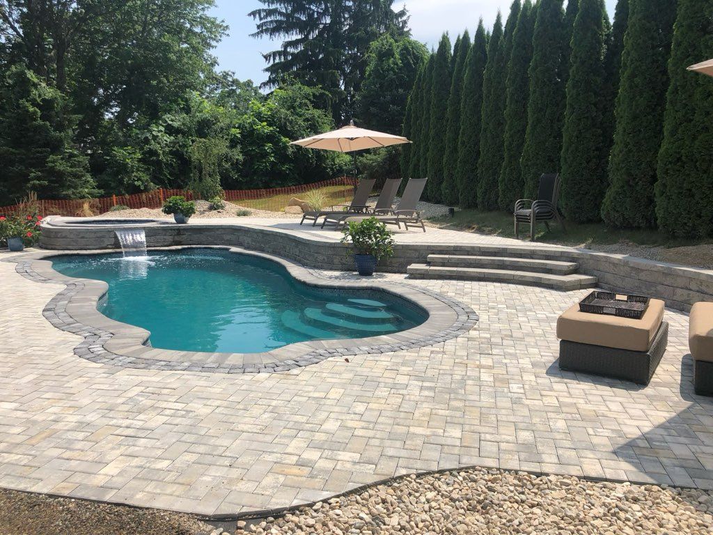 Backyard pool with stone patio, lounge chairs, umbrella, and tall hedges