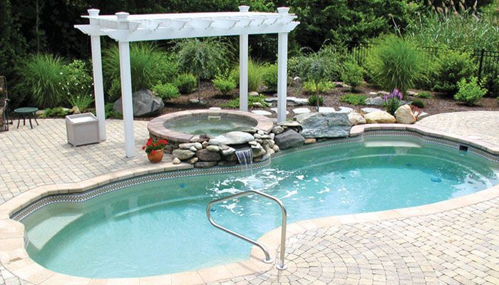 Backyard pool with turquoise water, stone waterfall, white pergola, and a metal pool handrail