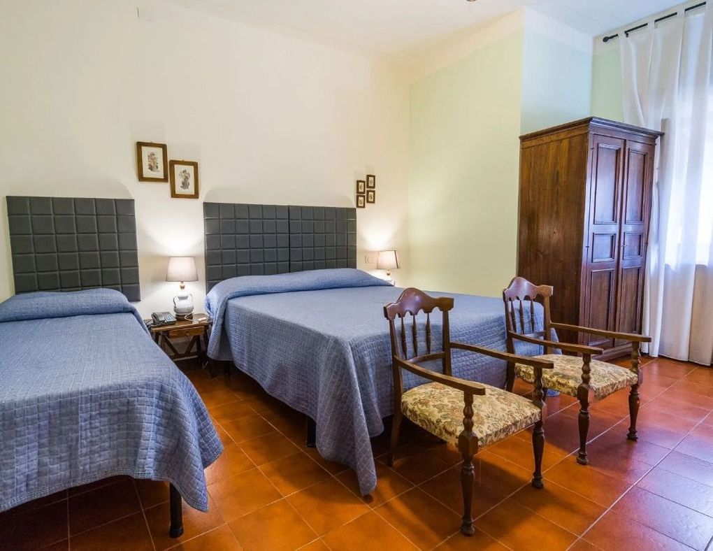 Camera da letto con due letti singoli, sedie in legno, un armadio e pavimento in piastrelle calde.