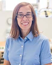 A woman wearing glasses and a blue shirt is smiling for the camera.