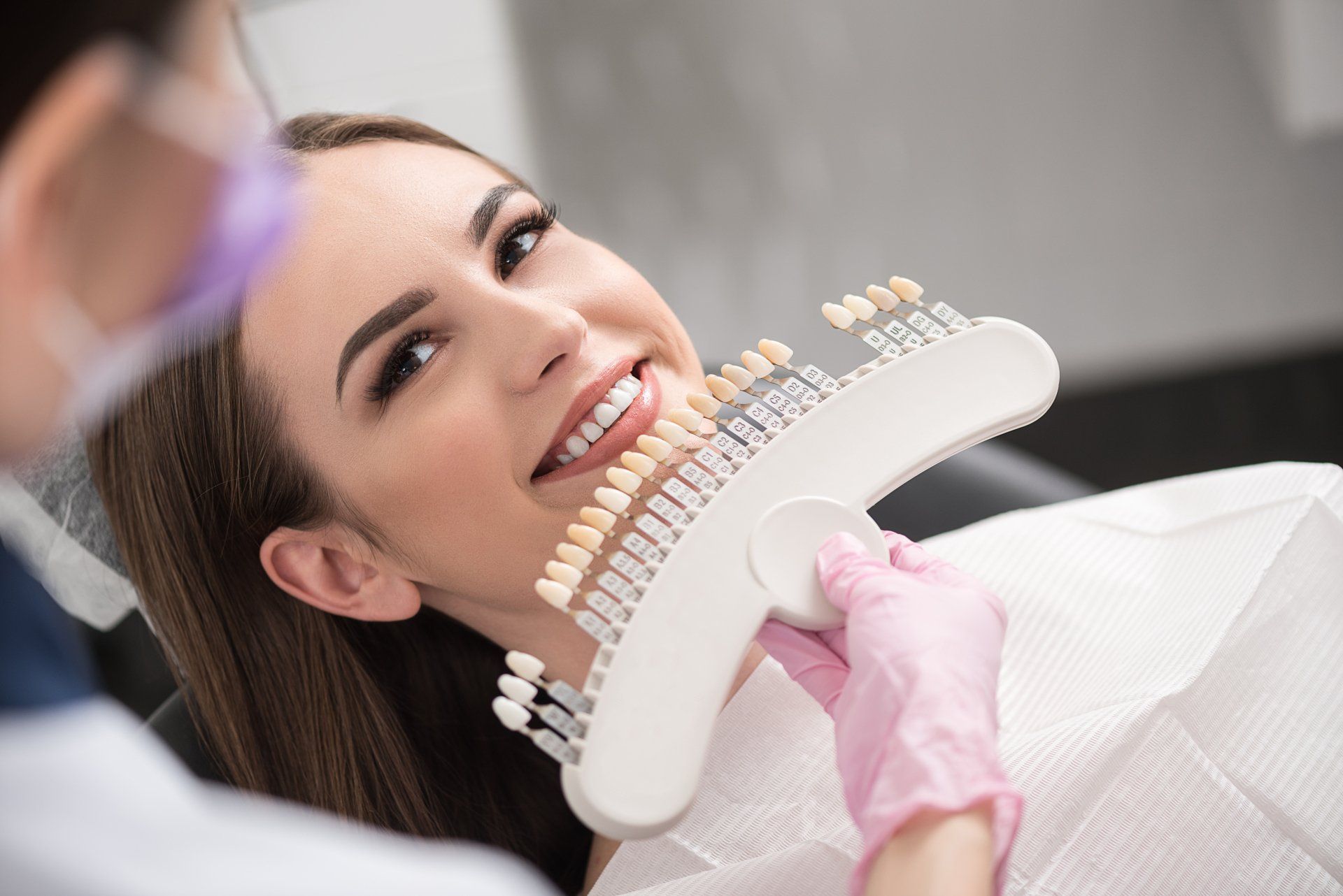 A woman is sitting in a dental chair while a dentist examines her teeth.