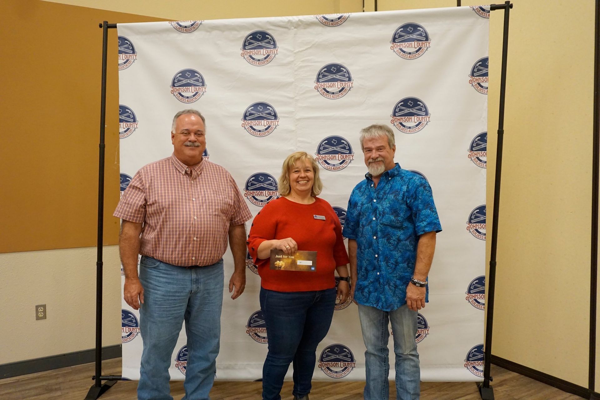 Three people posing in front of a branded backdrop, holding an award trophy.
