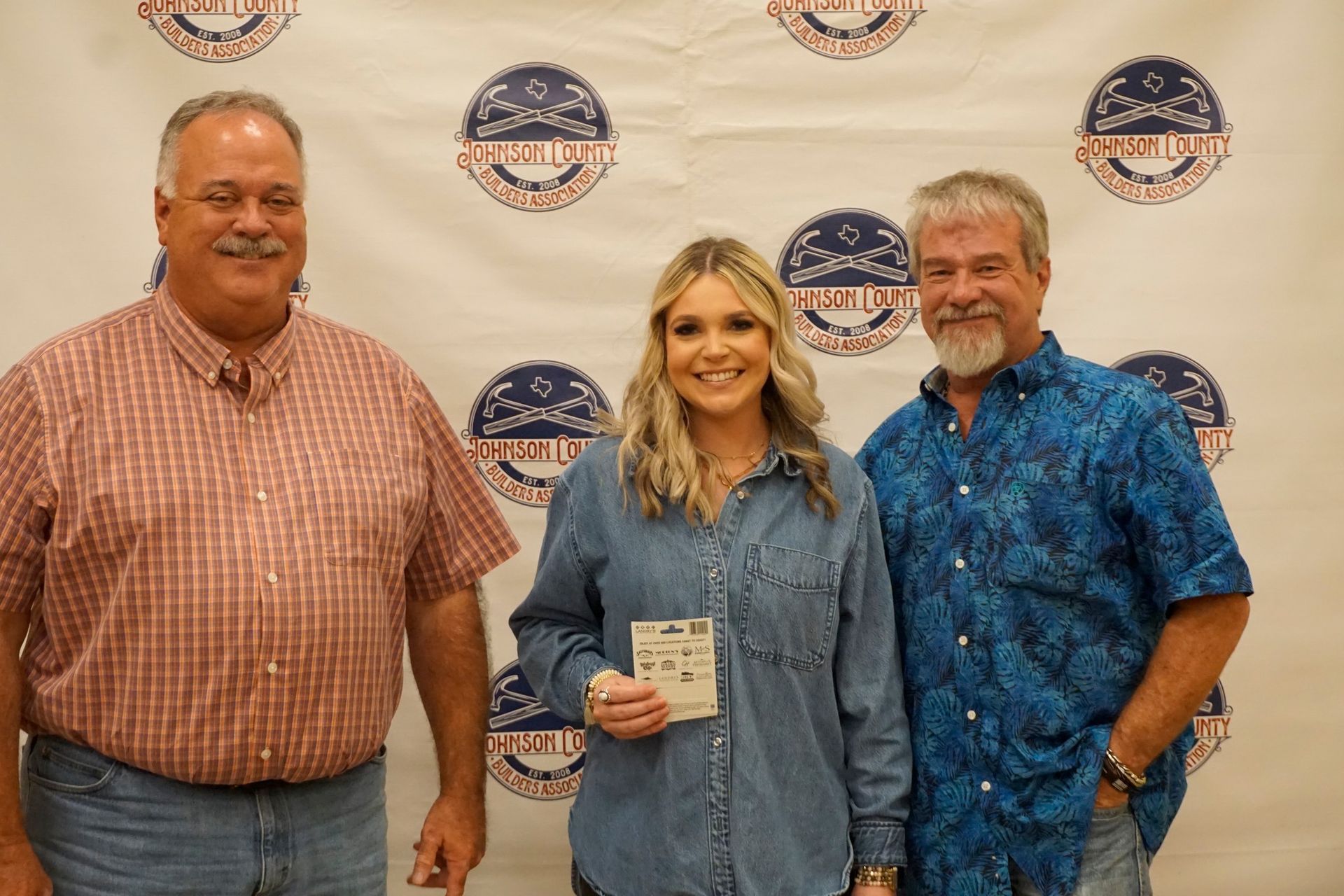 Three people posing at an awards backdrop, one holding a small plaque.