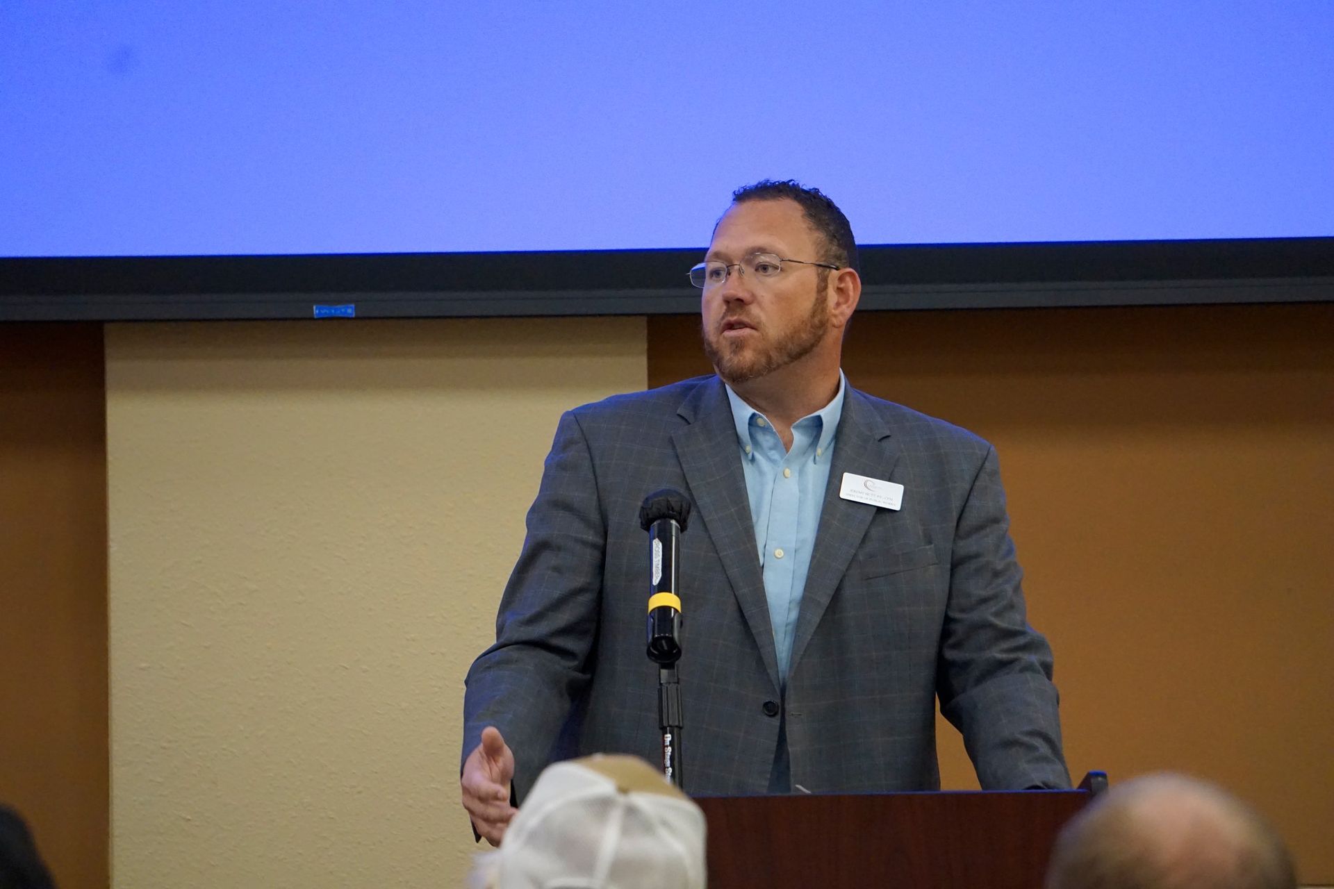 Man speaking at a podium in a conference room, with a blue screen behind him.