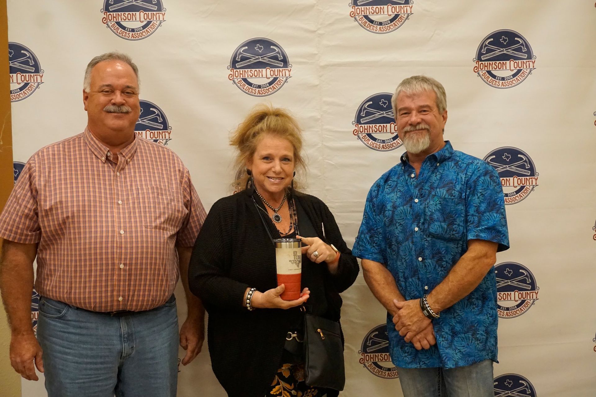 Three people posing with an award in front of a branded step-and-repeat backdrop
