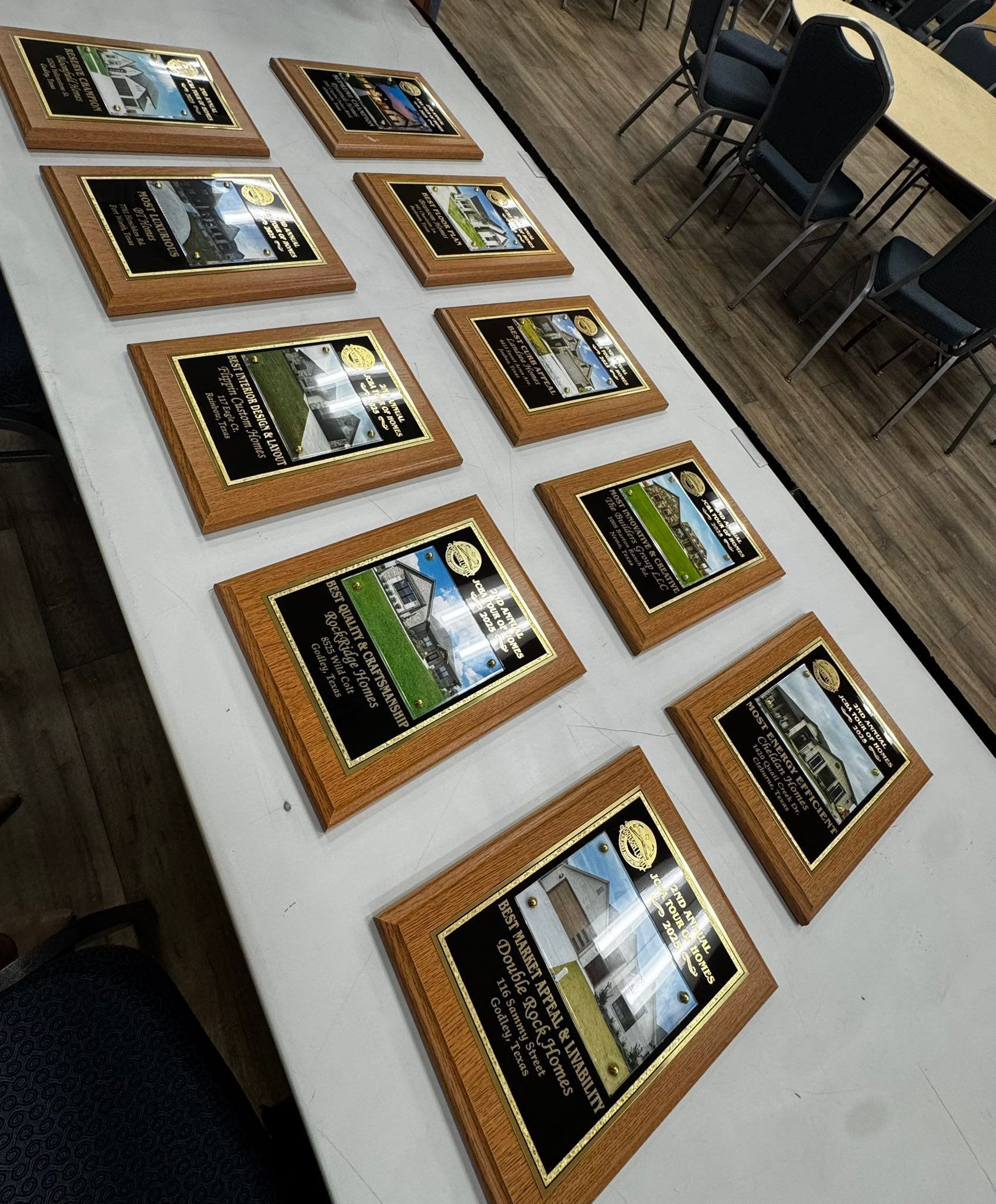 Framed photos and captions laid out on a white table beside a row of chairs on a wood floor.