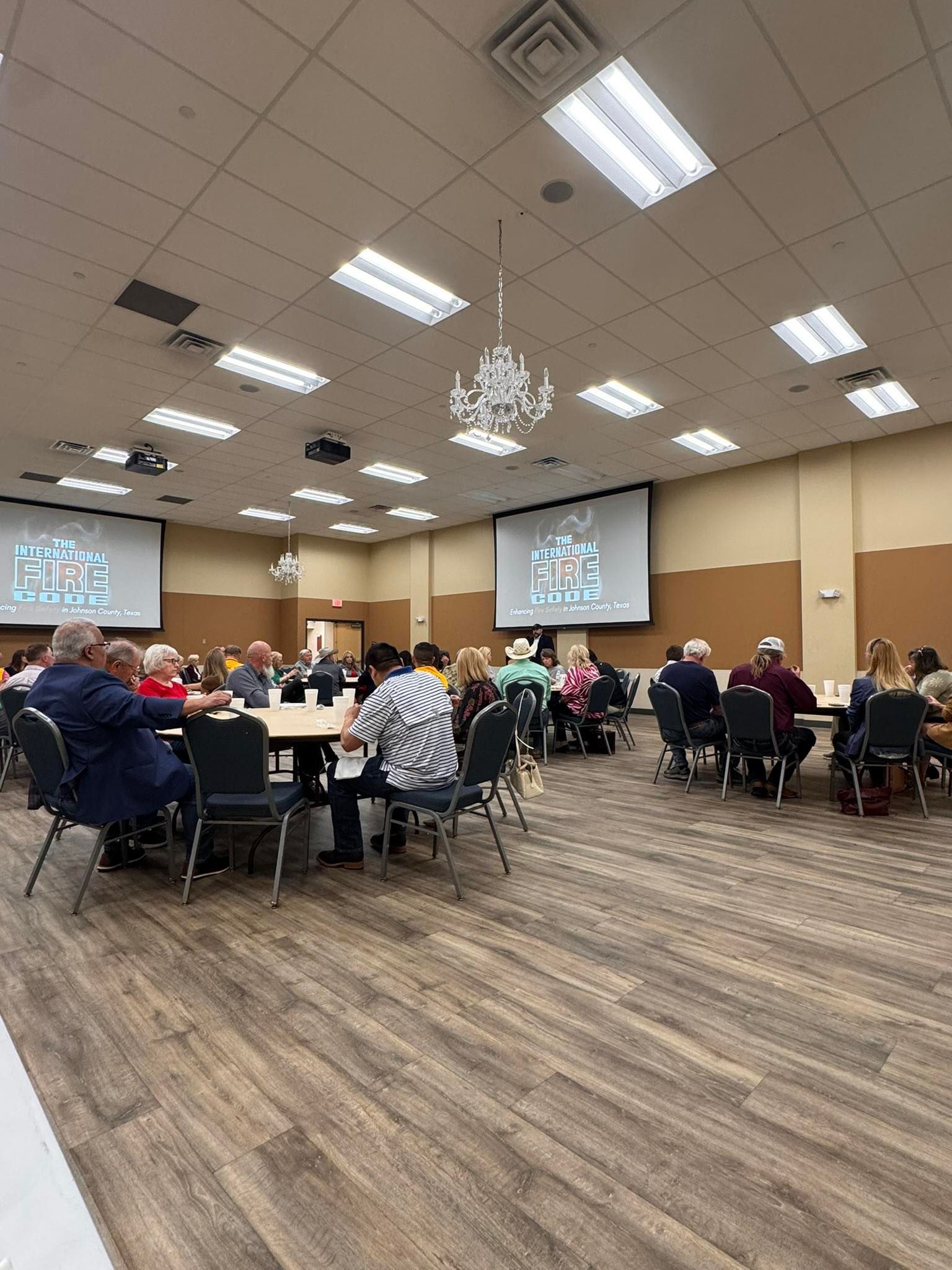 Conference room with people seated at round tables facing two projection screens during a presentation