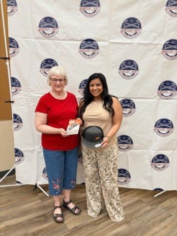 Two women posing at an event backdrop, one holding a round award plaque.