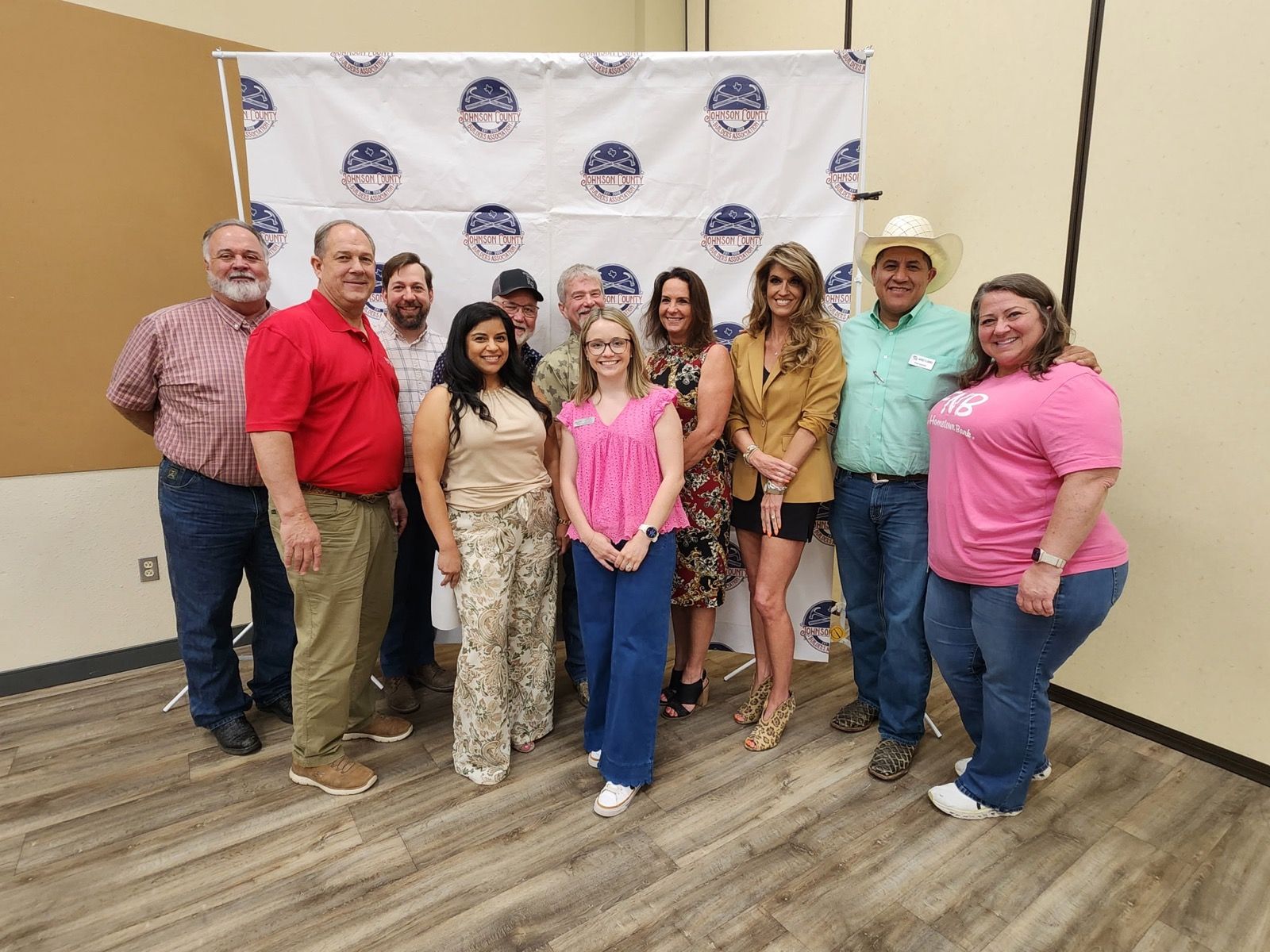 Group of people posing in front of a logo backdrop at an indoor event, smiling and standing together