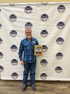 A man in a plaid shirt is holding a framed picture in front of a white wall.