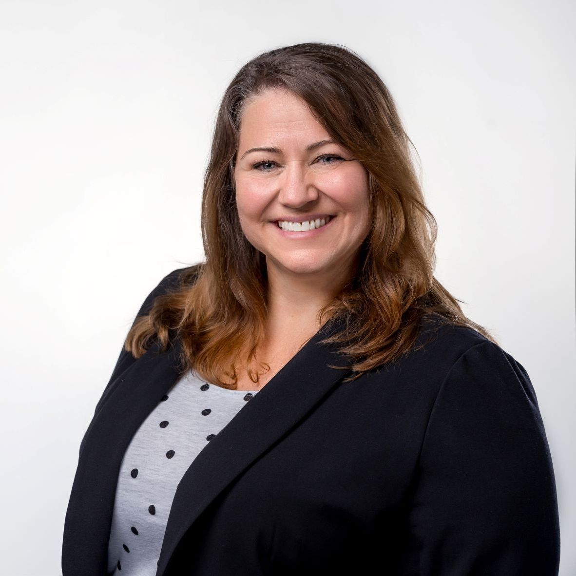 A woman in a black jacket and polka dot shirt is smiling for the camera.