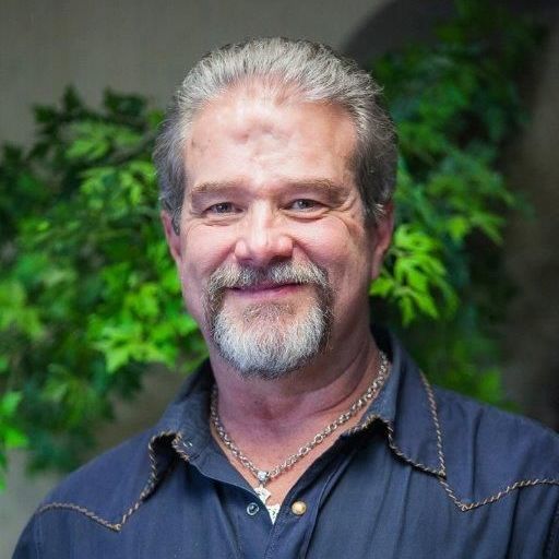 A man with a beard and a chain around his neck is smiling for the camera.