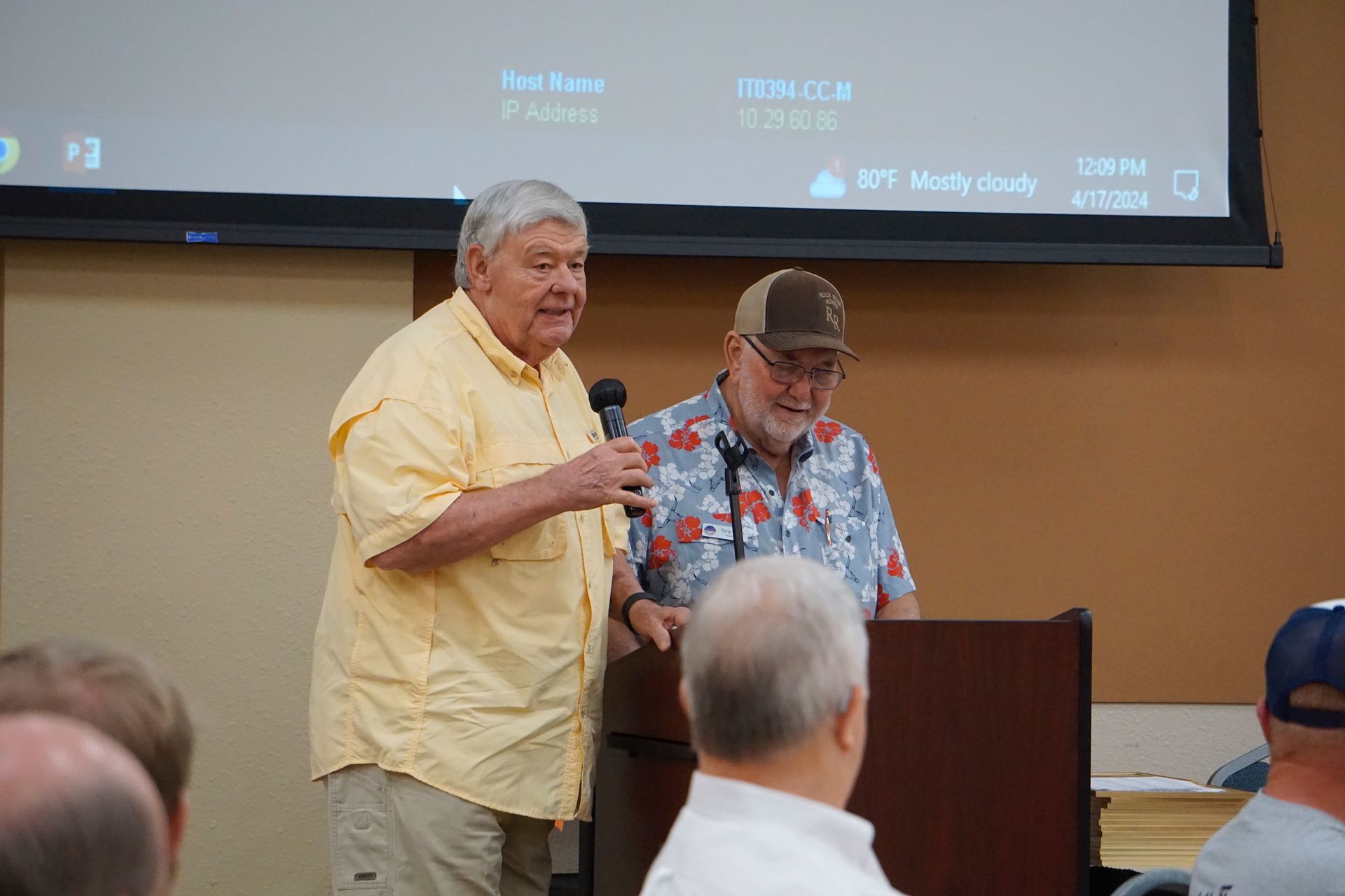 Two men are standing at a podium giving a presentation to a group of people.