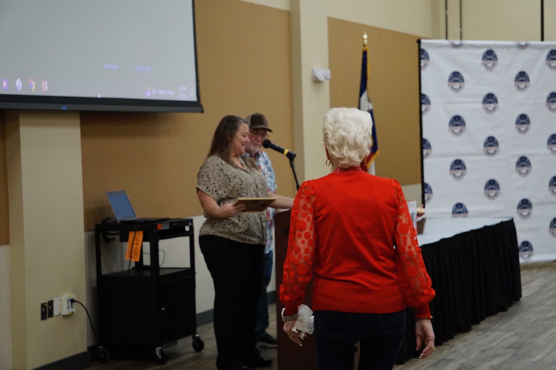 A woman in a red sweater is standing in front of a microphone in a room.