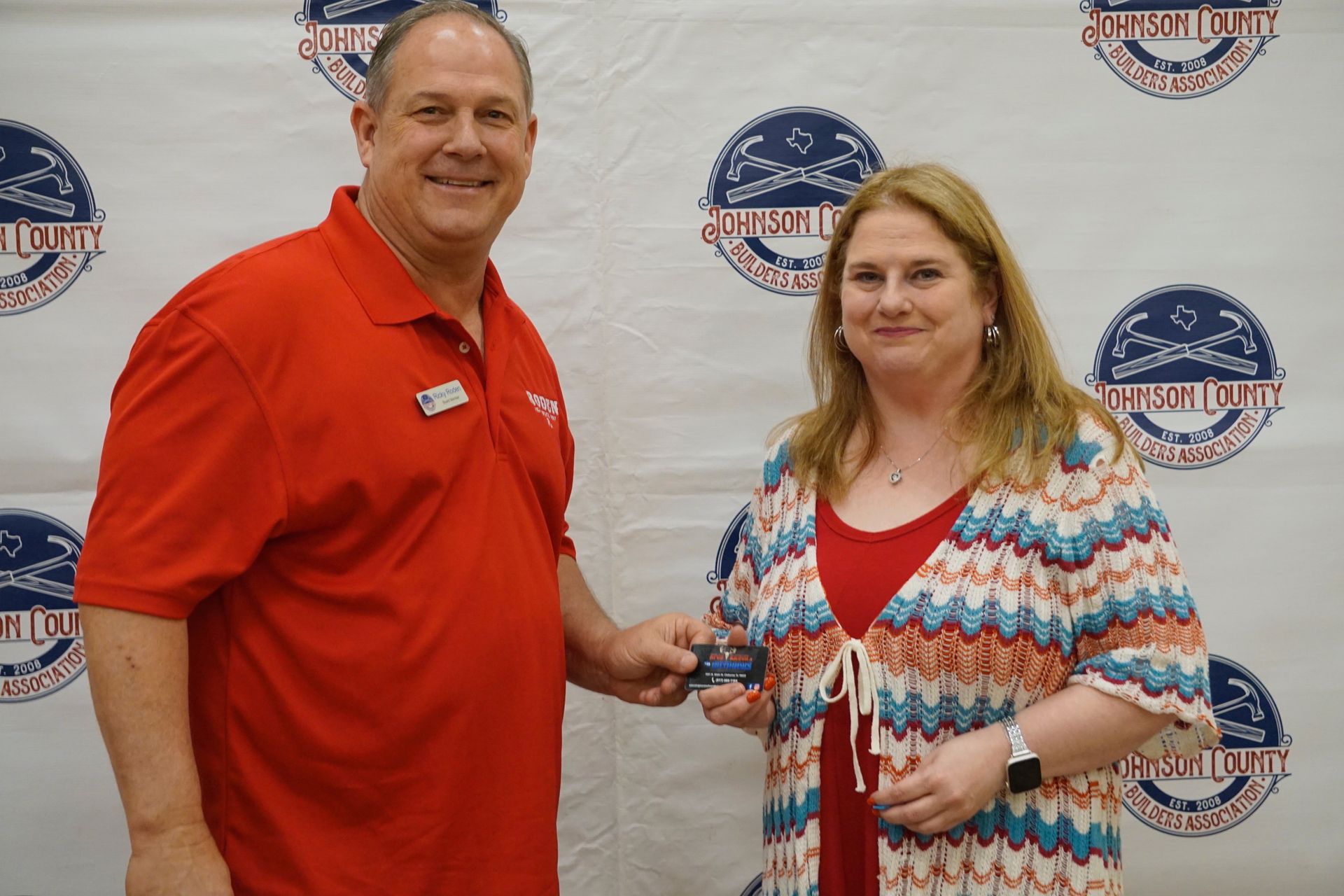 A man in a red shirt is shaking hands with a woman in a colorful dress.