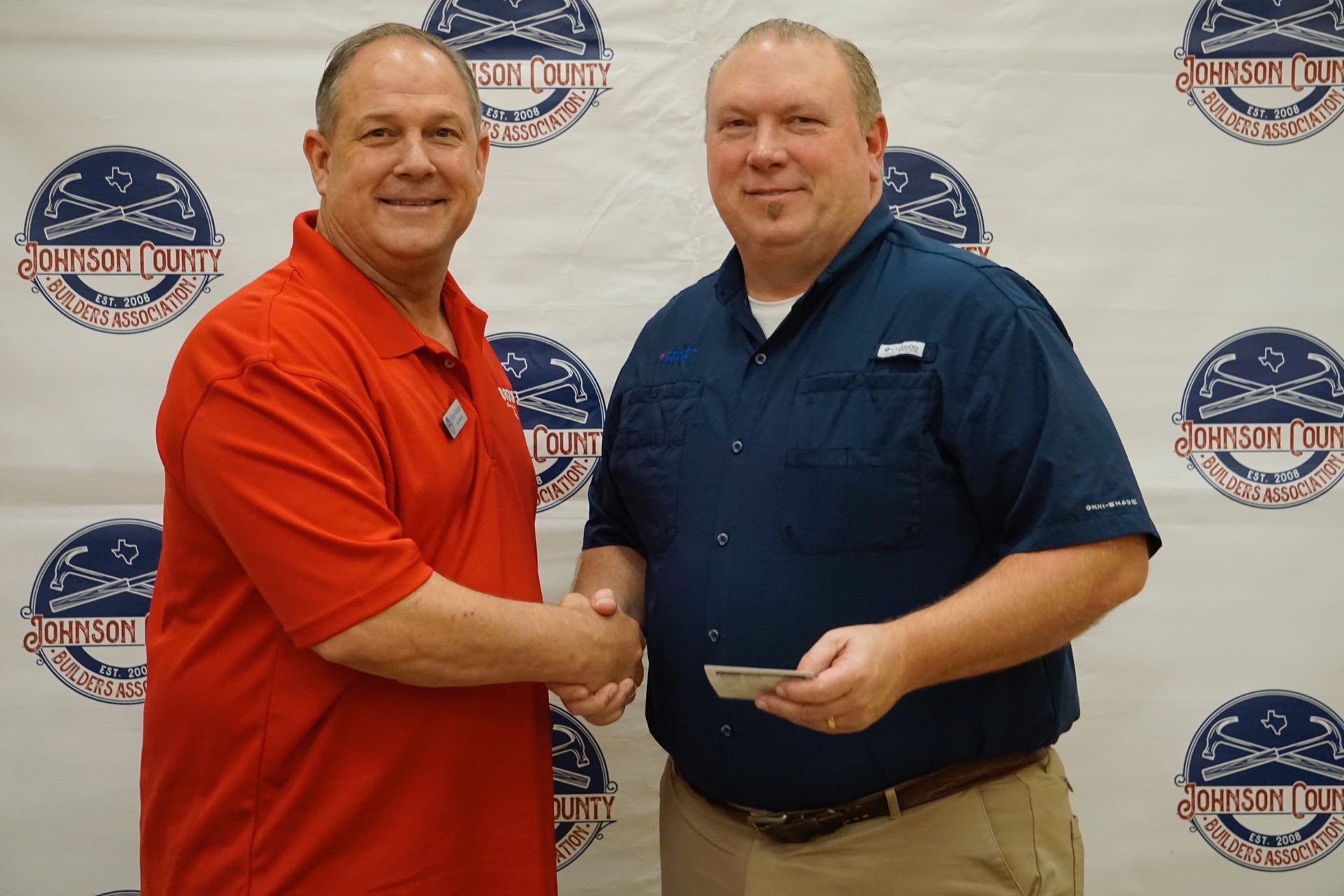 A man in a red shirt is shaking hands with another man in a blue shirt
