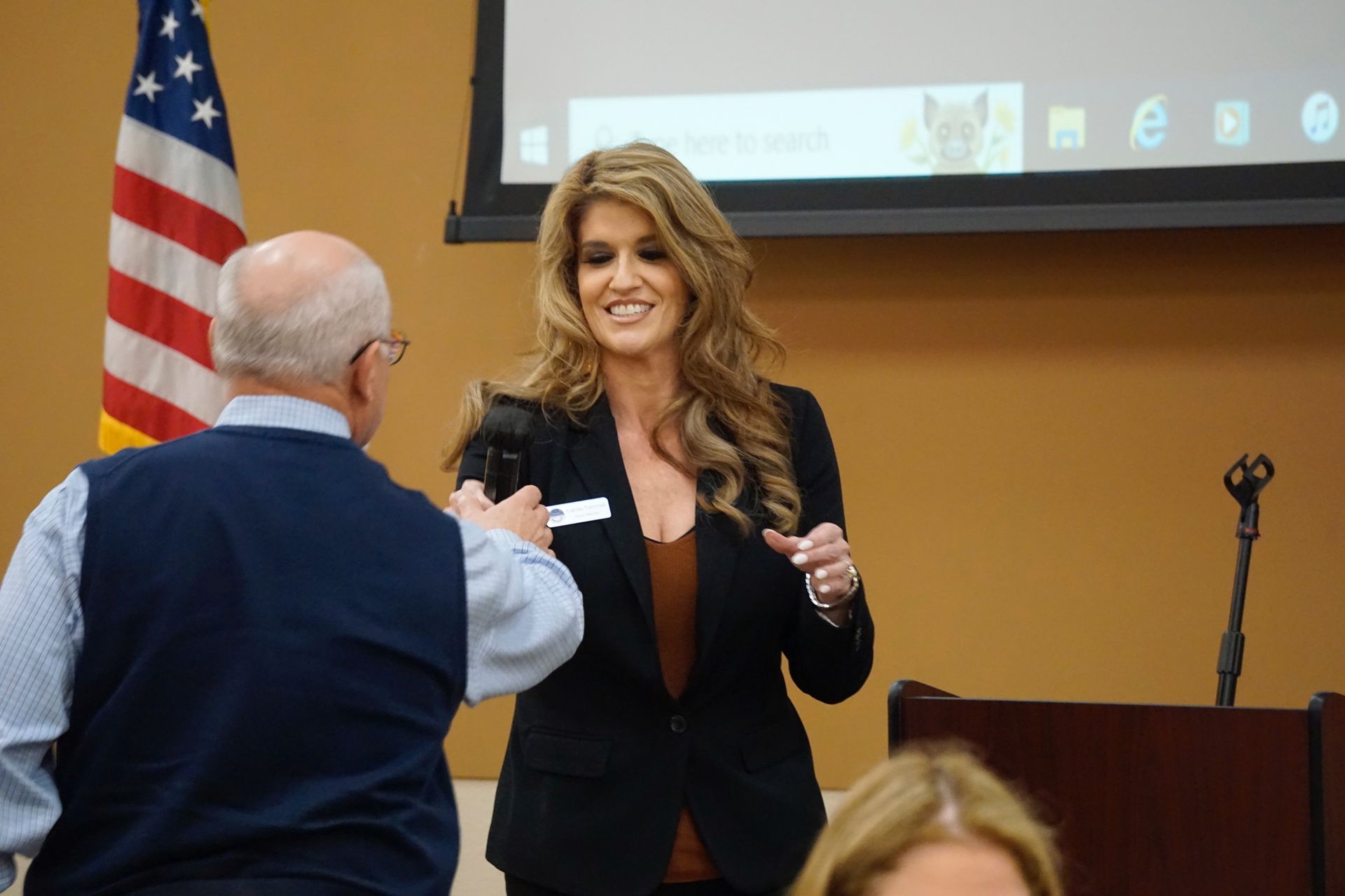 A woman is talking to a man in front of an american flag.