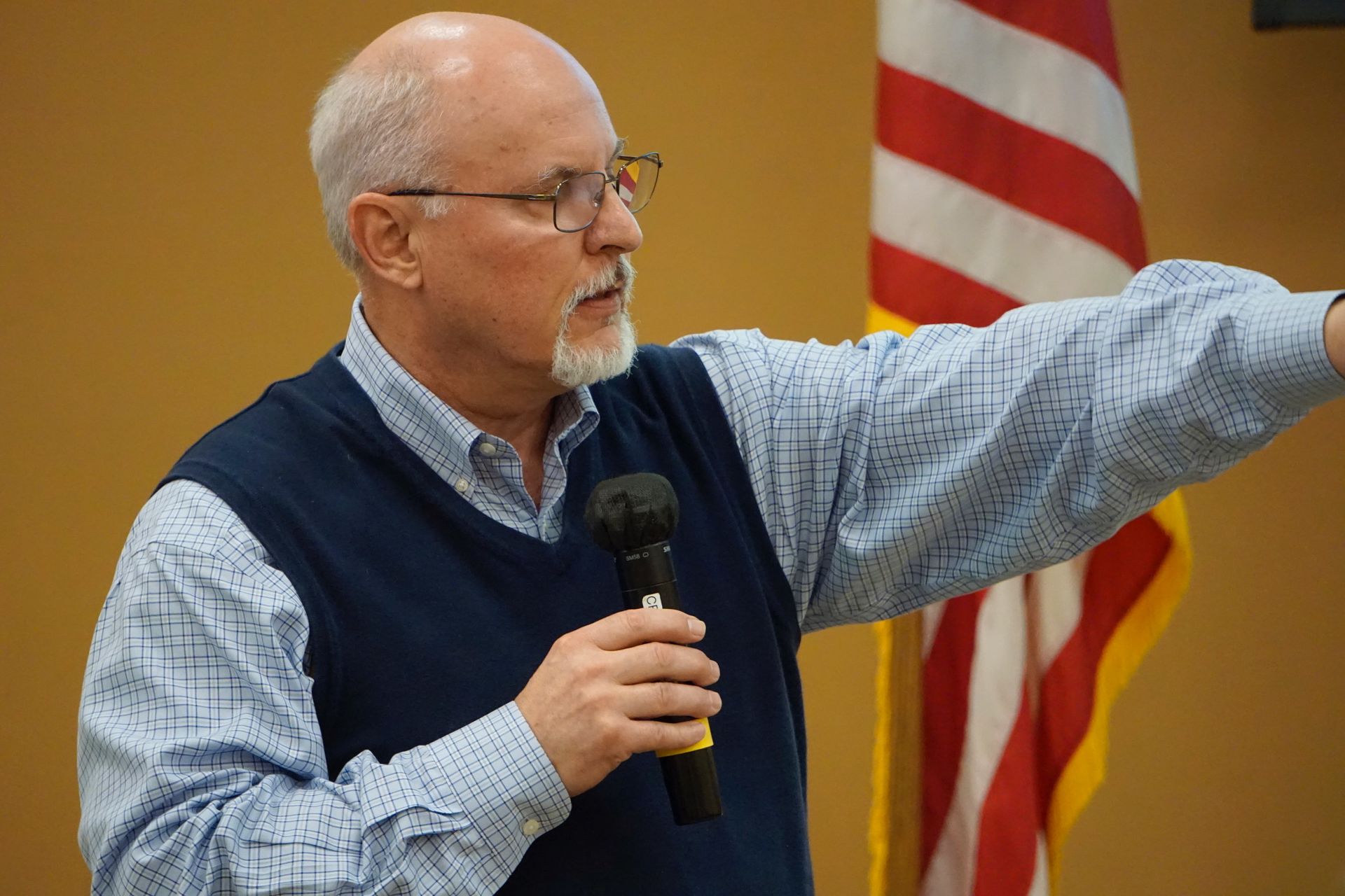 A man is holding a microphone in front of an american flag.