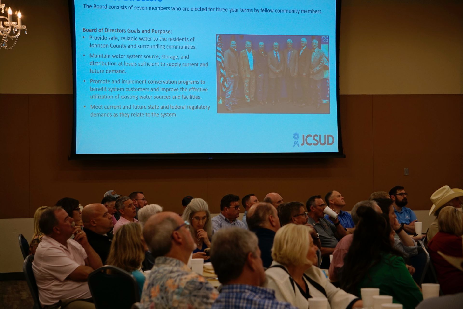 A group of people are sitting in front of a large screen.