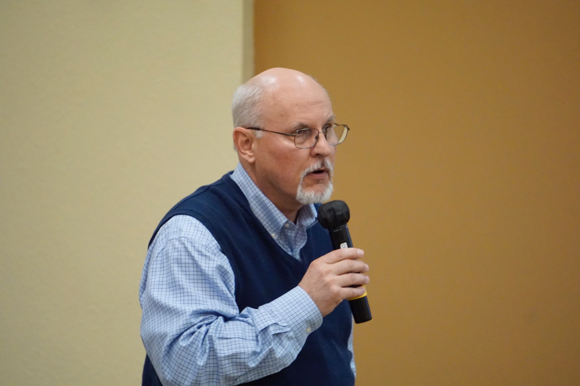 A man with glasses and a beard is holding a microphone and talking into it.