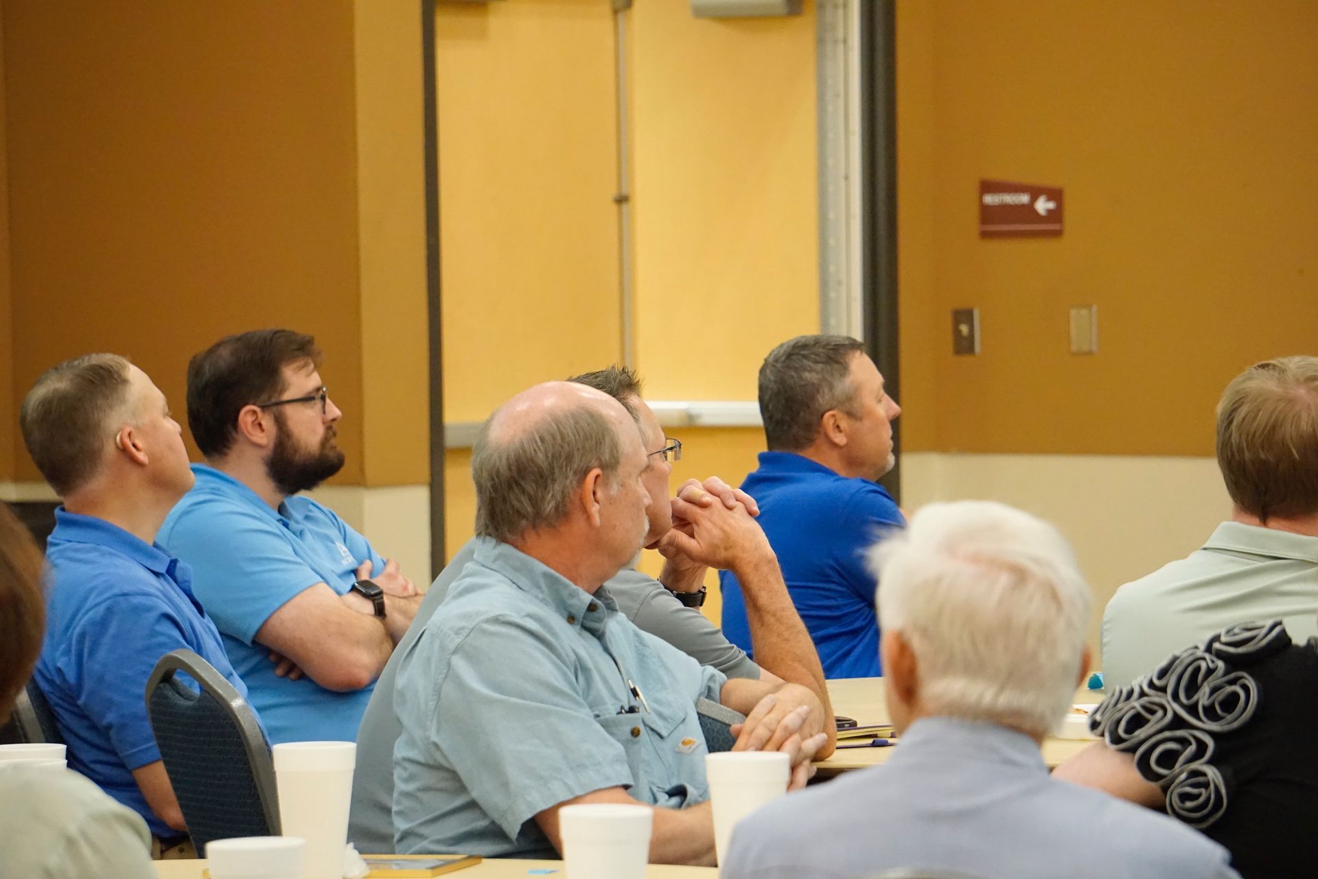 A group of men are sitting at a table listening to a presentation.