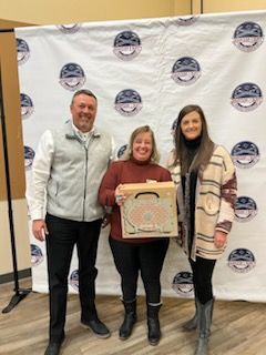 A man and two women are standing next to each other holding a pizza box.