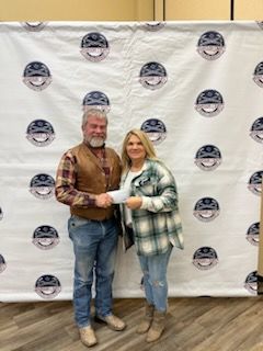 A man and a woman are standing in front of a wall holding a check.