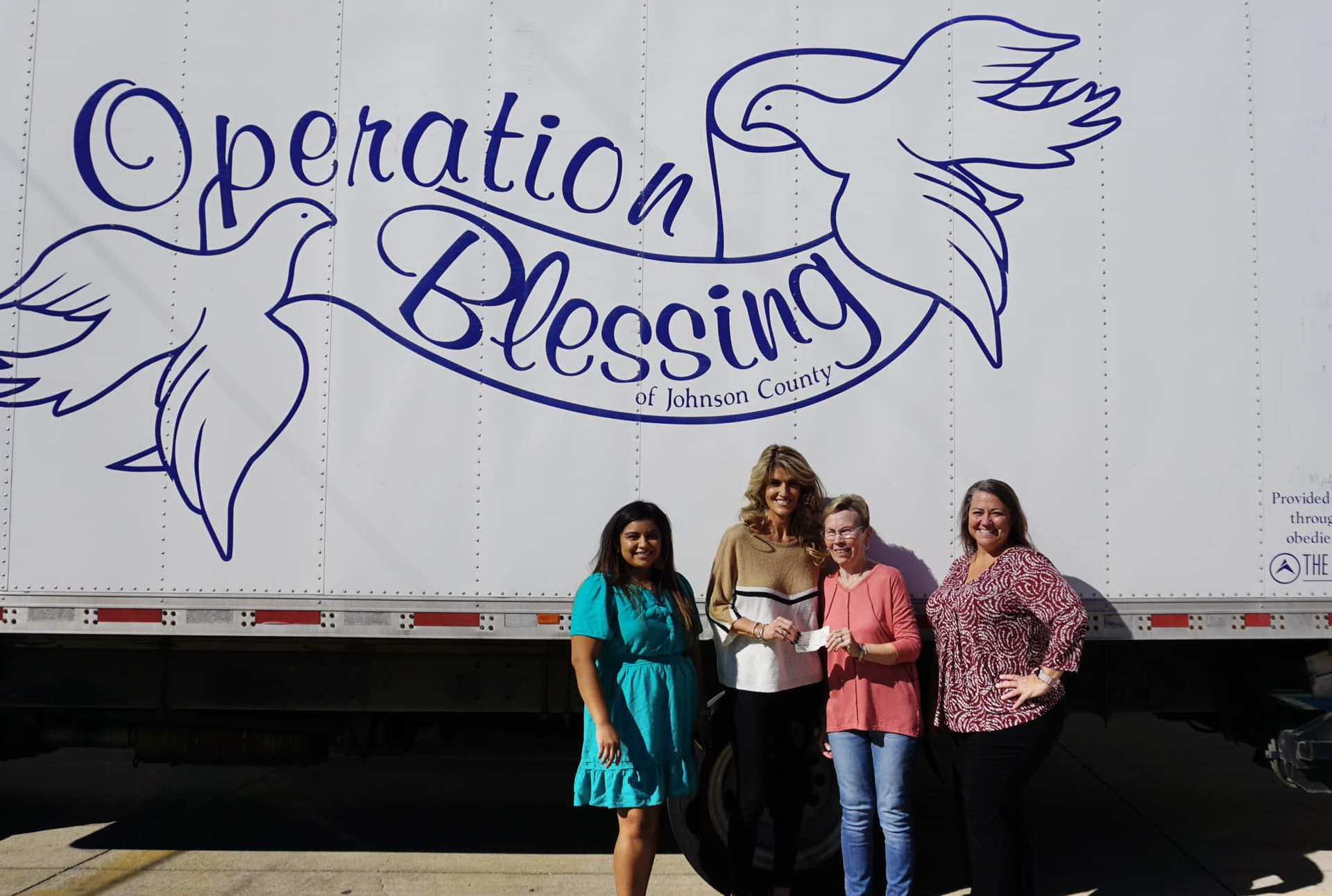 Four people standing before an Operation Blessing truck with blue dove graphics and logo