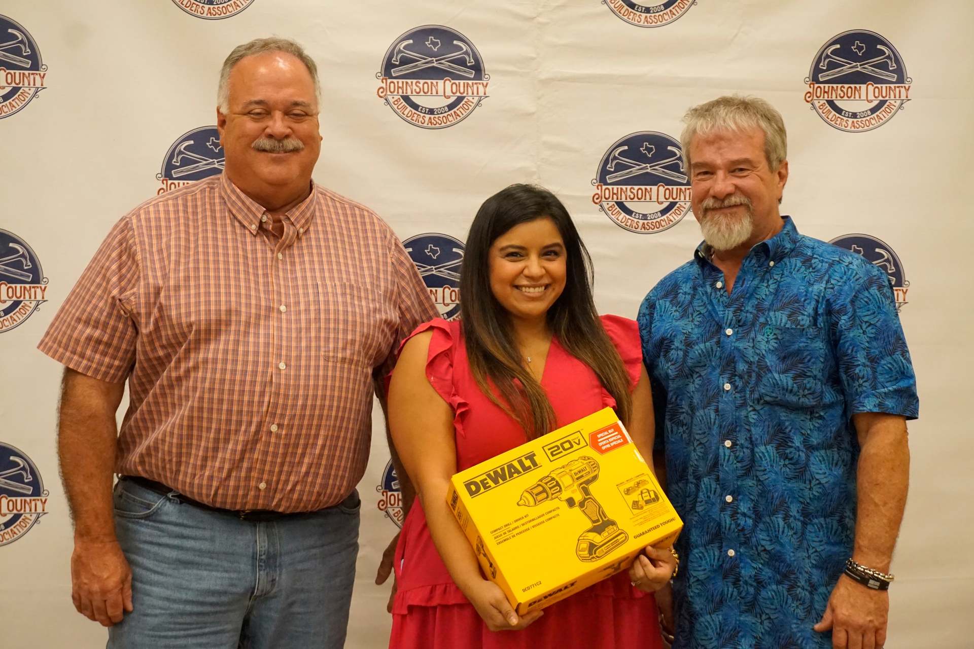 Three people posing at an event, holding a yellow award plaque in front of a logo backdrop