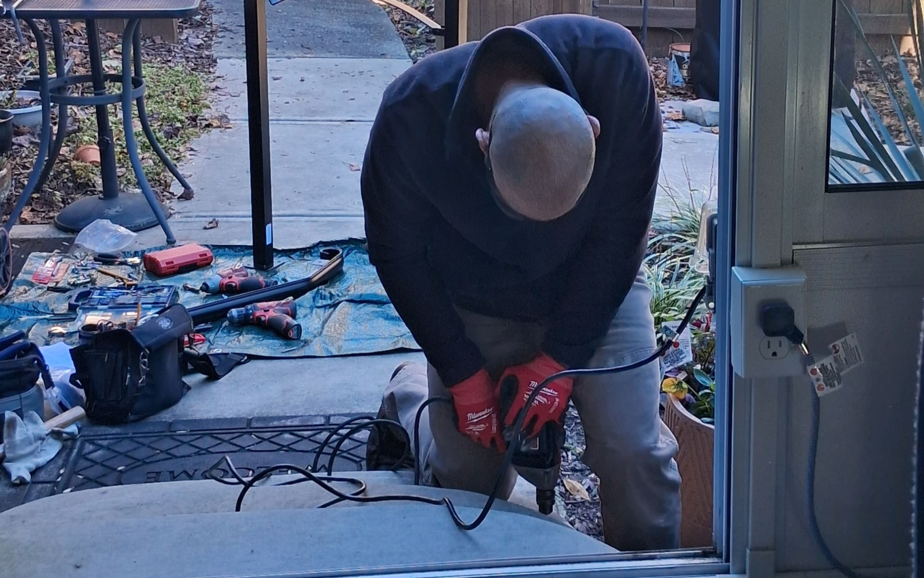 Person using a red chainsaw to cut wood on a porch with scattered tools and debris.