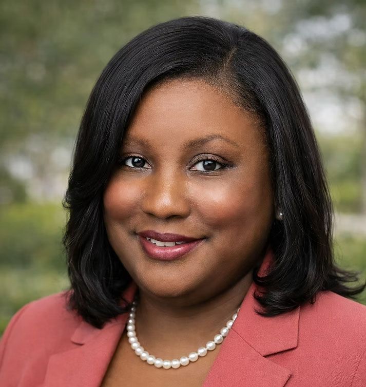 Portrait of a smiling woman in a coral blazer and pearl necklace outdoors