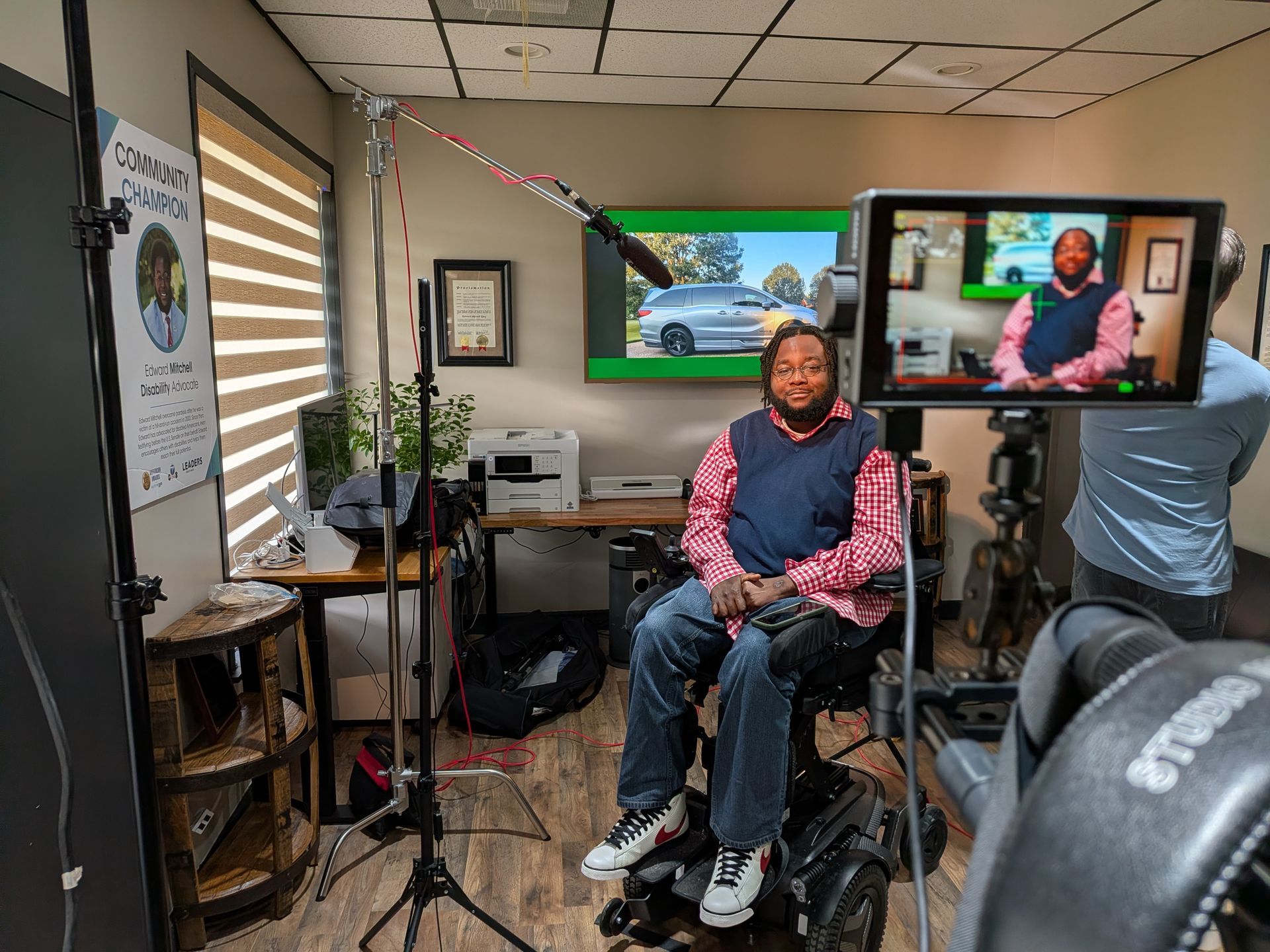 Person seated in a small studio, speaking on camera with two monitors and a camera operator nearby