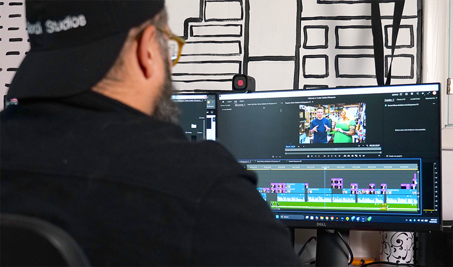 Person editing video on dual monitors in a studio workspace, with a timeline and preview screen visible.