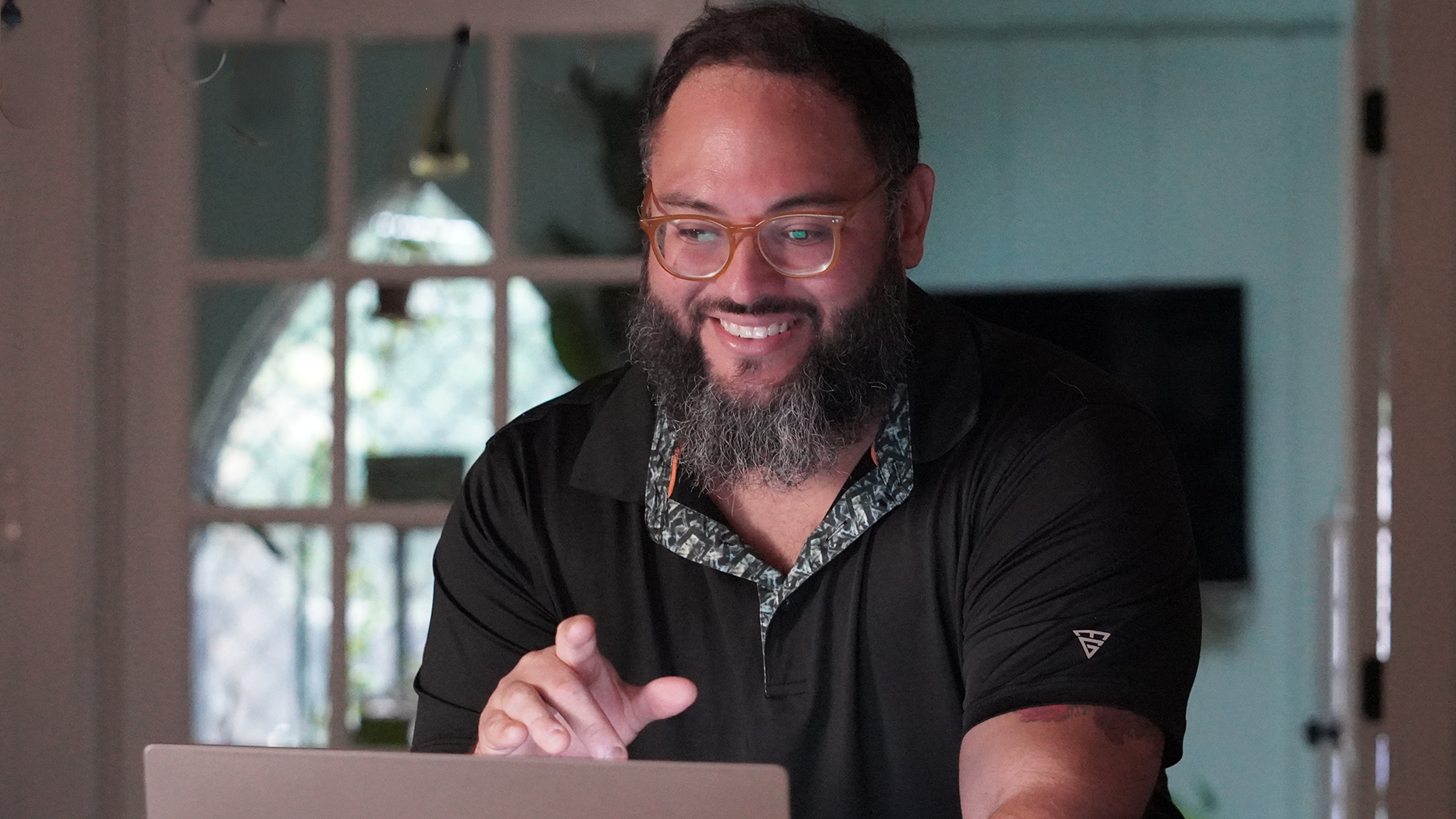 Smiling man in glasses using a laptop at a desk in a softly lit room