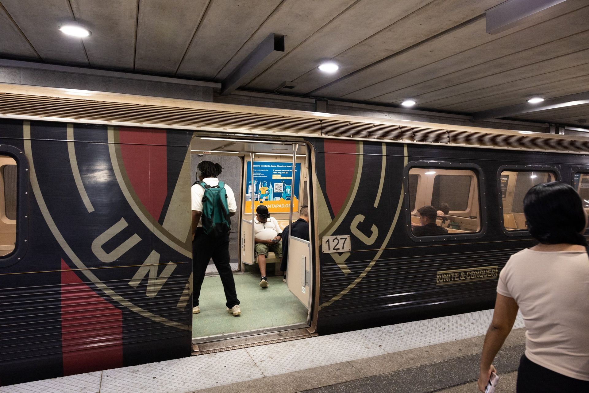 People boarding a decorated subway train at an underground station, with one person walking in.