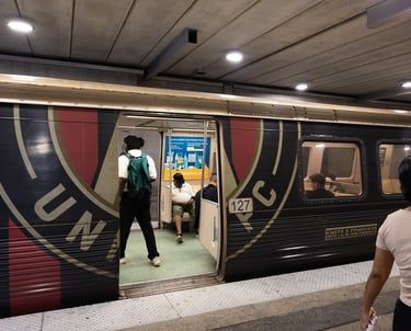 Train at a station with open doors, showing passengers boarding and a large “UN” logo on the side.