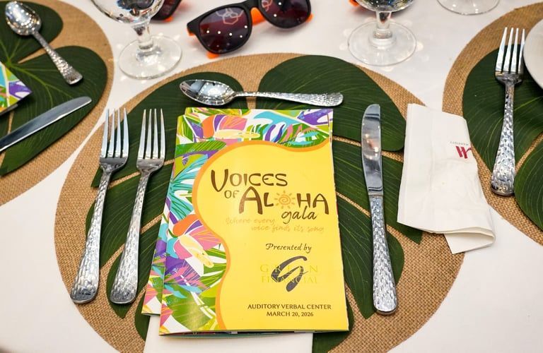 Table setting with green placemats, silverware, sunglasses, and a yellow “Voices of” program card.