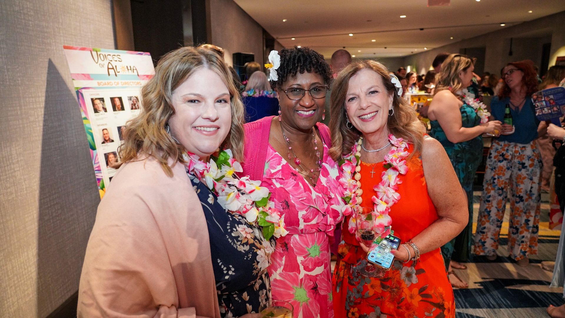 Three women smiling and posing at an indoor event with a poster board in the background