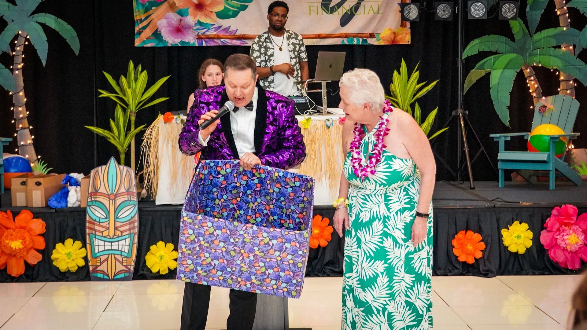 Two people at a decorated event stage, holding patterned cloths and looking down together