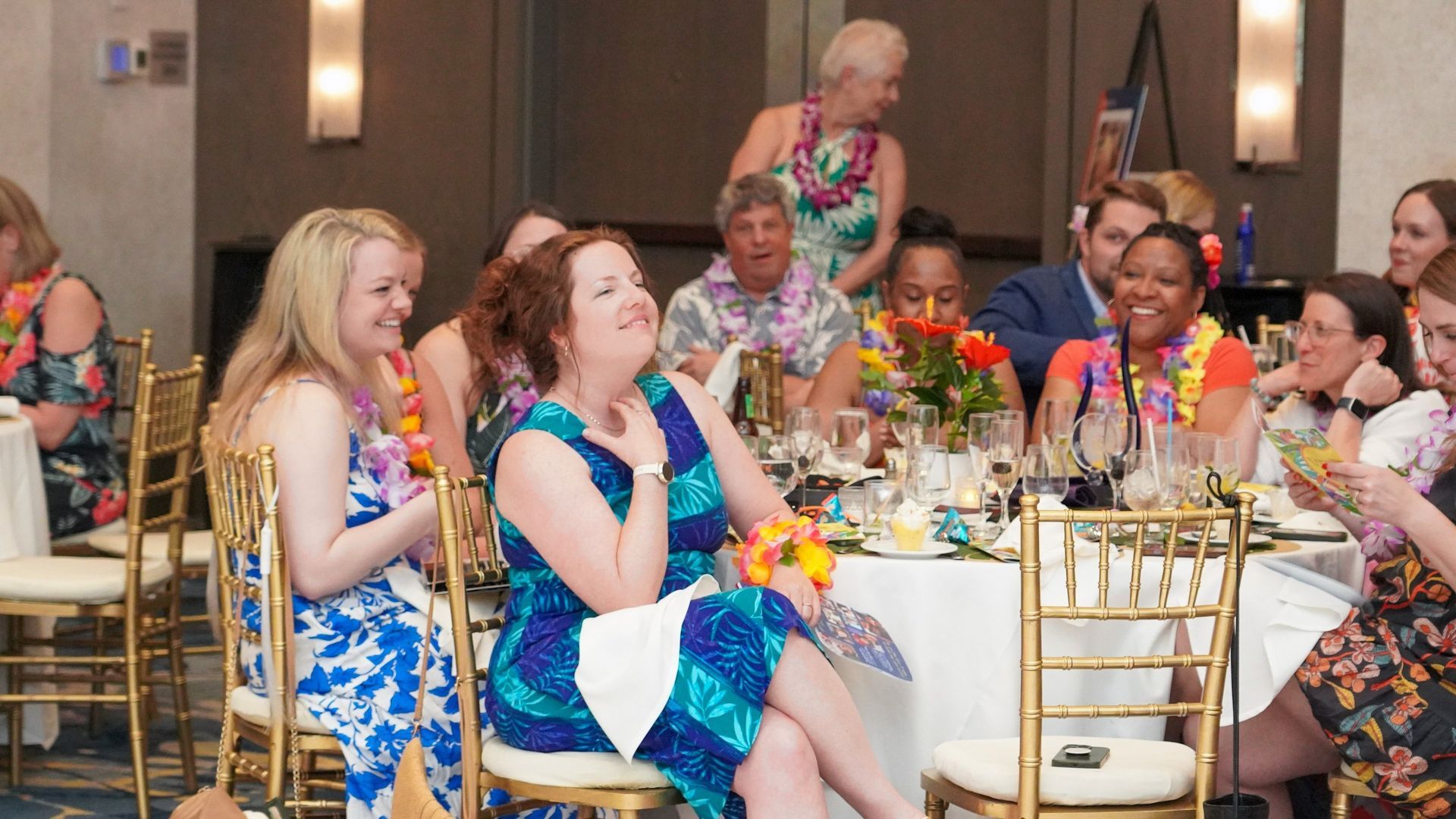 Guests seated at a decorated banquet table, listening and chatting in a warmly lit ballroom