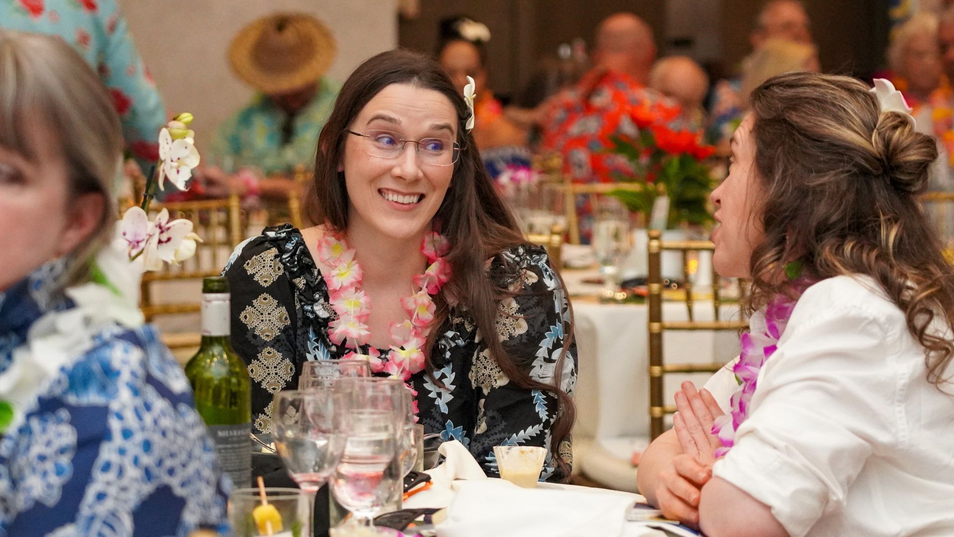 Three people chatting at a decorated table during a festive indoor gathering
